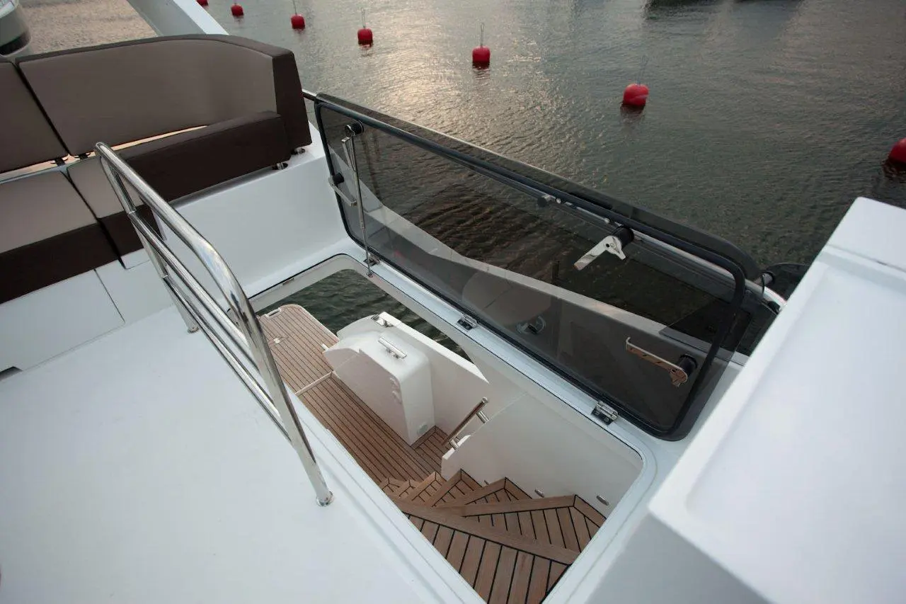 View from above showing a stairway leading below deck on a yacht, with a glass hatch and adjacent seating area.