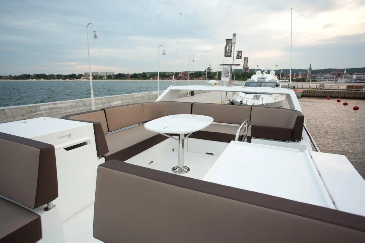 Luxury yacht deck with cushioned seating and a round table overlooking calm water and a distant shoreline.