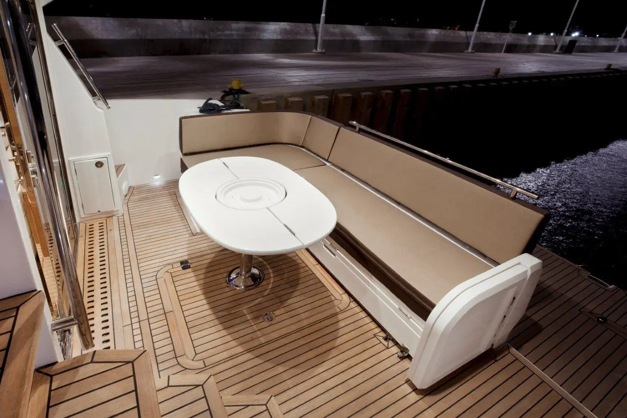 Sea yacht deck featuring a cushioned seating area with a round table, illuminated by night, overlooking a calm harbor.