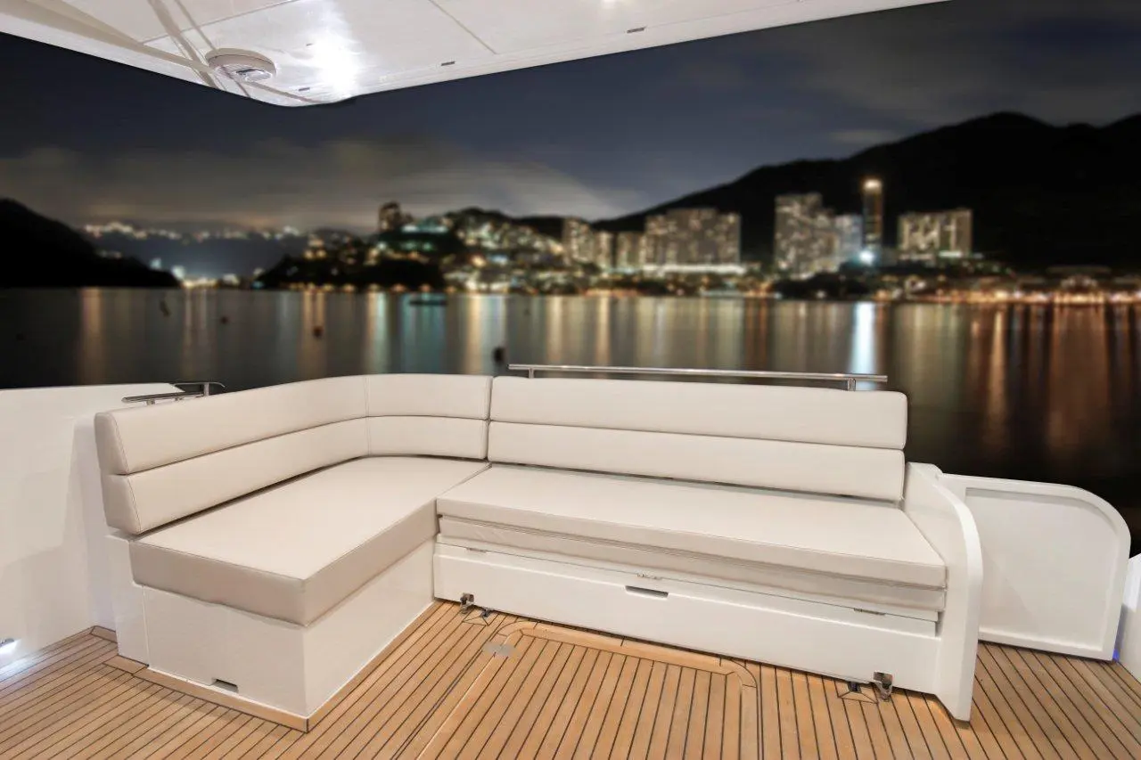Luxury yacht interior featuring a stylish white seating area, with a scenic waterfront view of illuminated buildings at night.