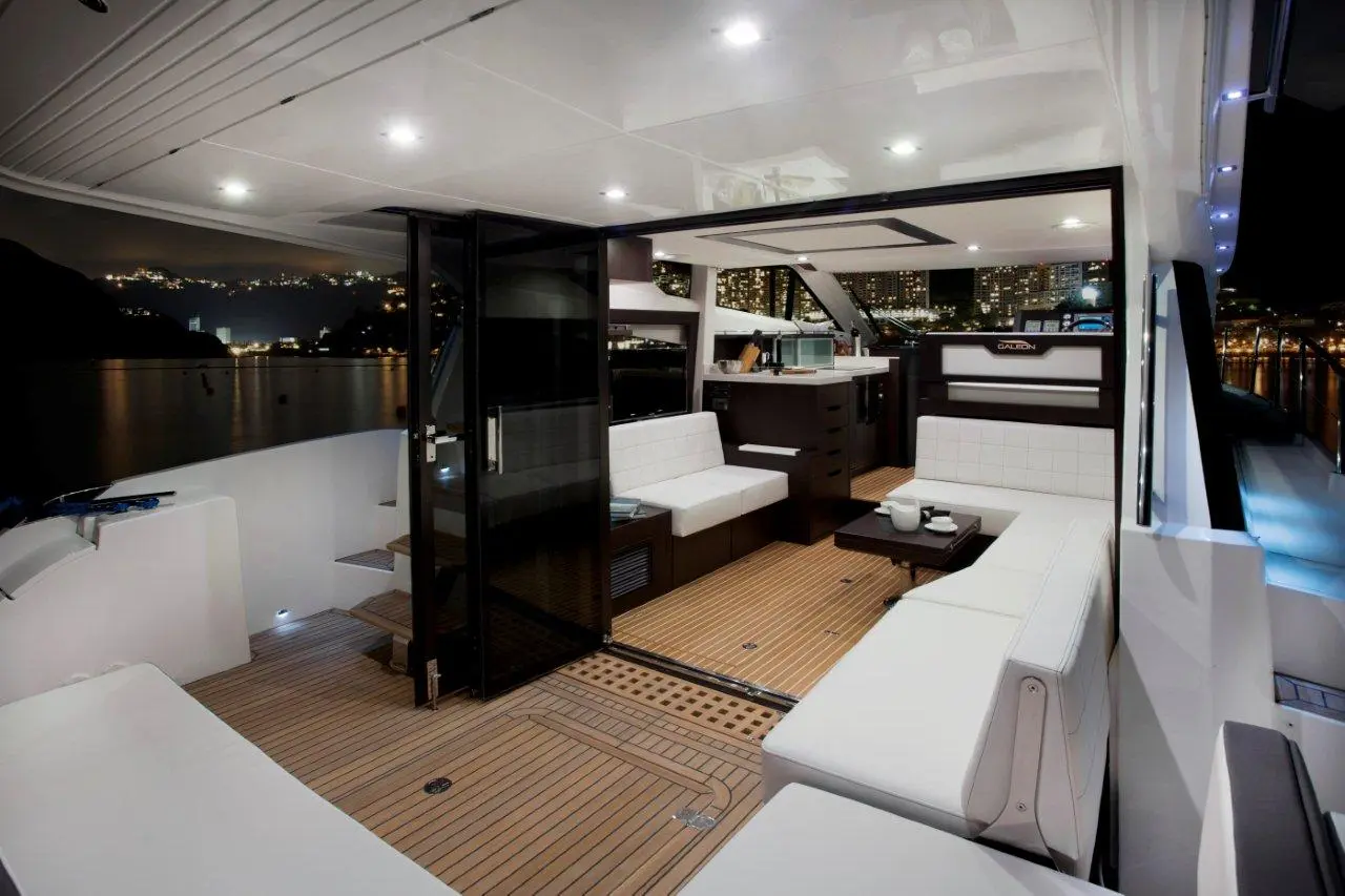 Modern yacht interior at night featuring sleek seating, a dining table, and a view of city lights reflecting on water.
