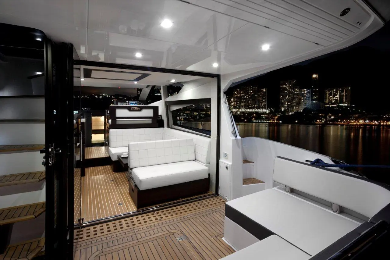 Modern yacht interior at night, featuring plush seating, wooden flooring, and a view of city lights outside the windows.