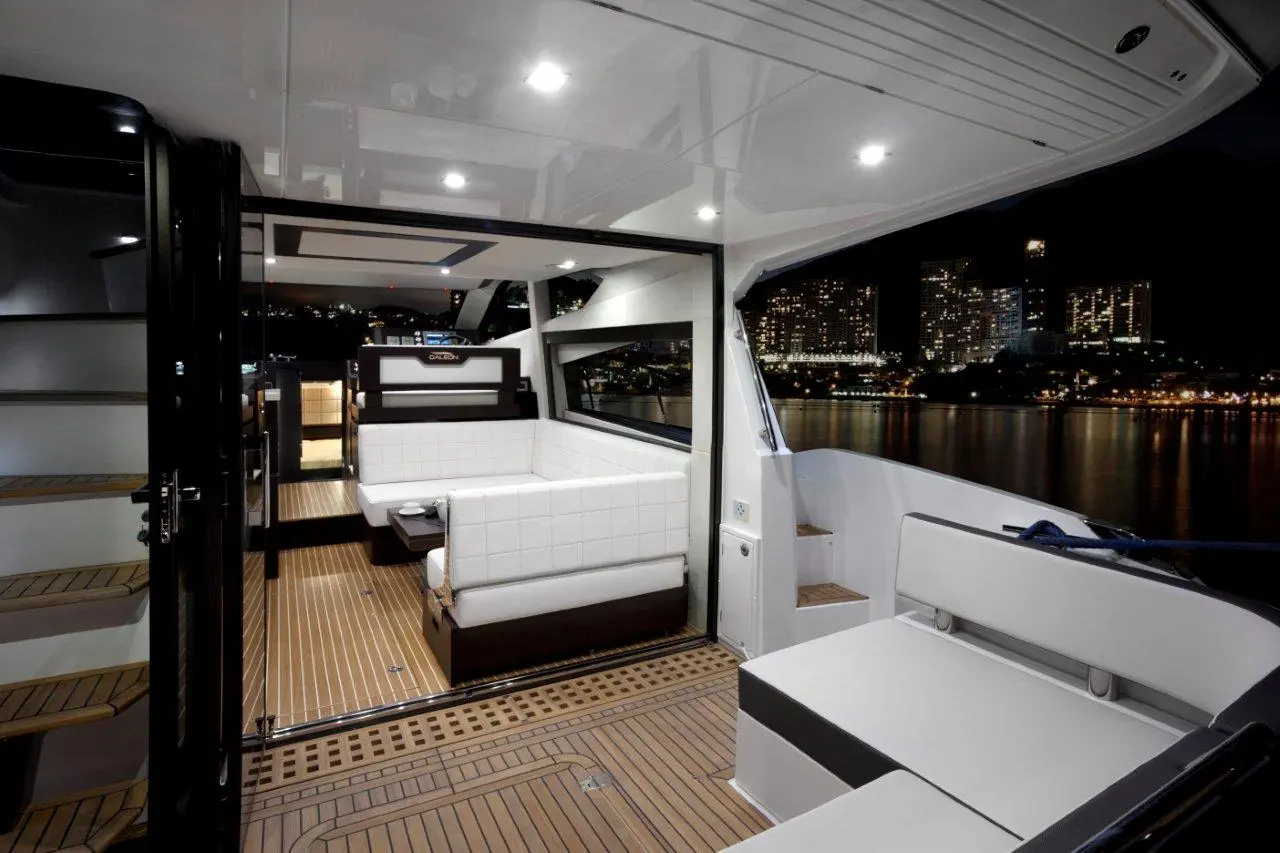 Modern boat interior at night with sleek furnishings, wooden floors, and a city skyline visible through large windows.