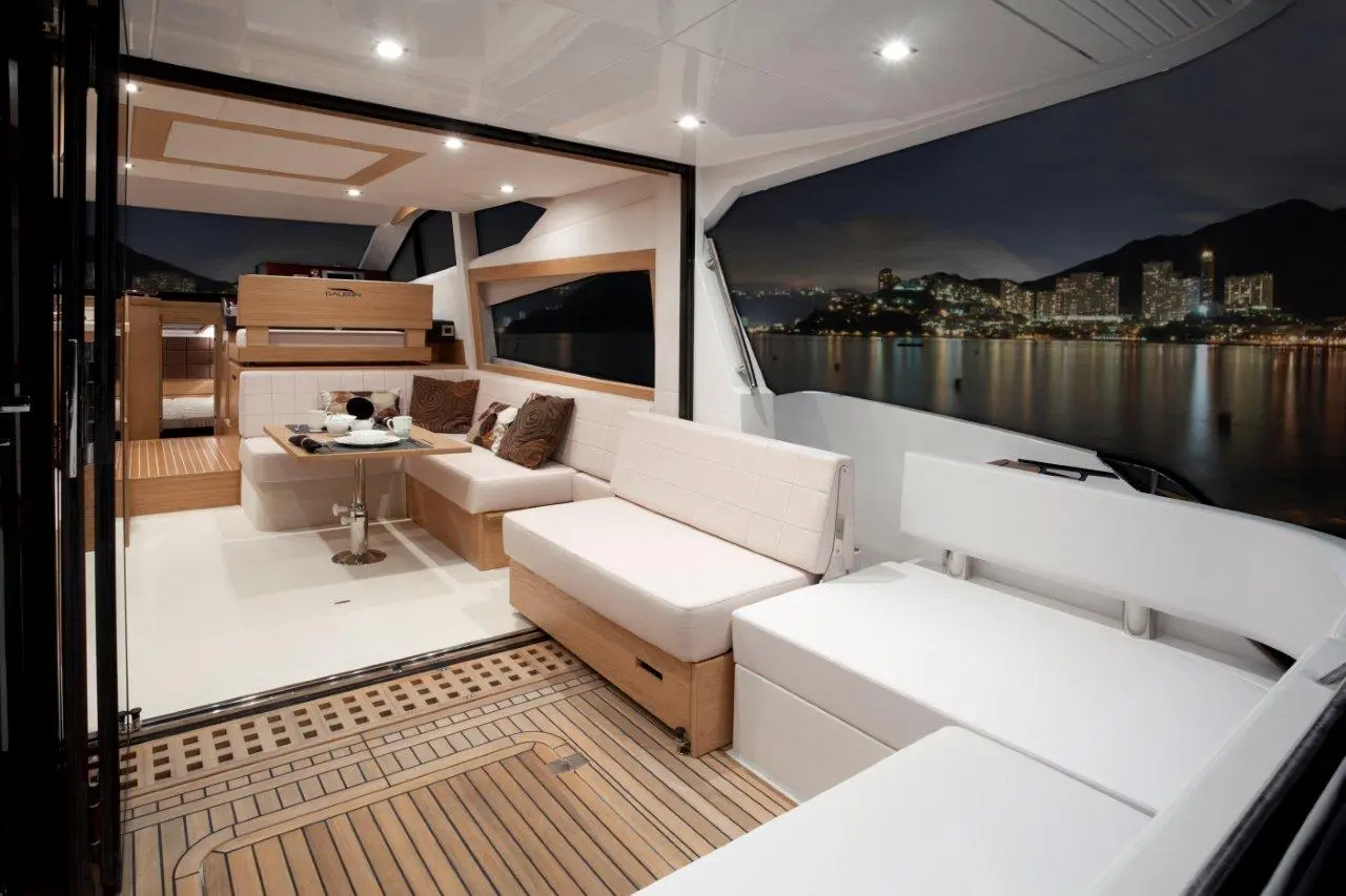 Luxurious yacht interior at night, featuring modern seating, a table set for meals, and a scenic city skyline view.