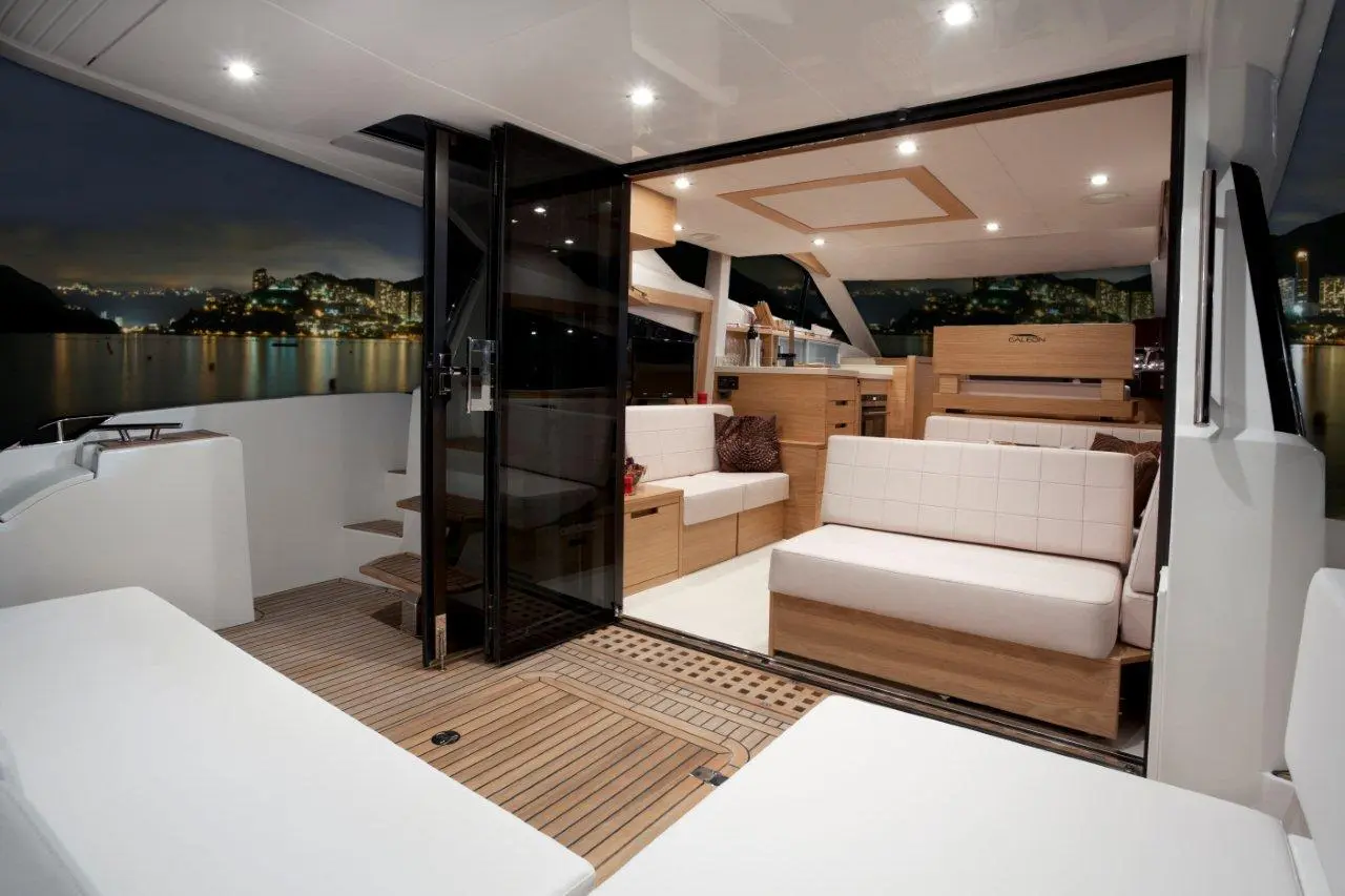A luxurious yacht interior at night, featuring modern furnishings, large glass doors, and a scenic city view.