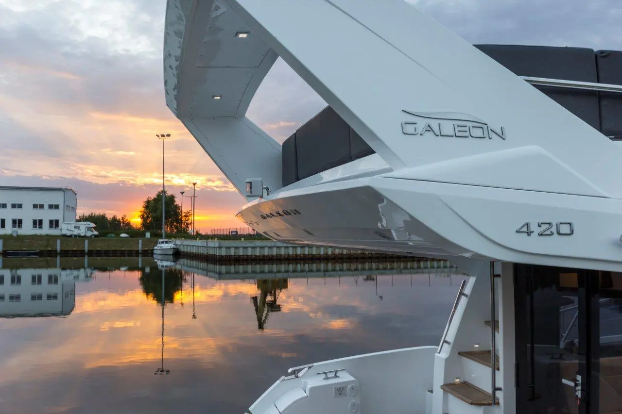 Galeon 420 yacht docked at sunset, reflecting in the water with a cloudy sky and a marina in the background.