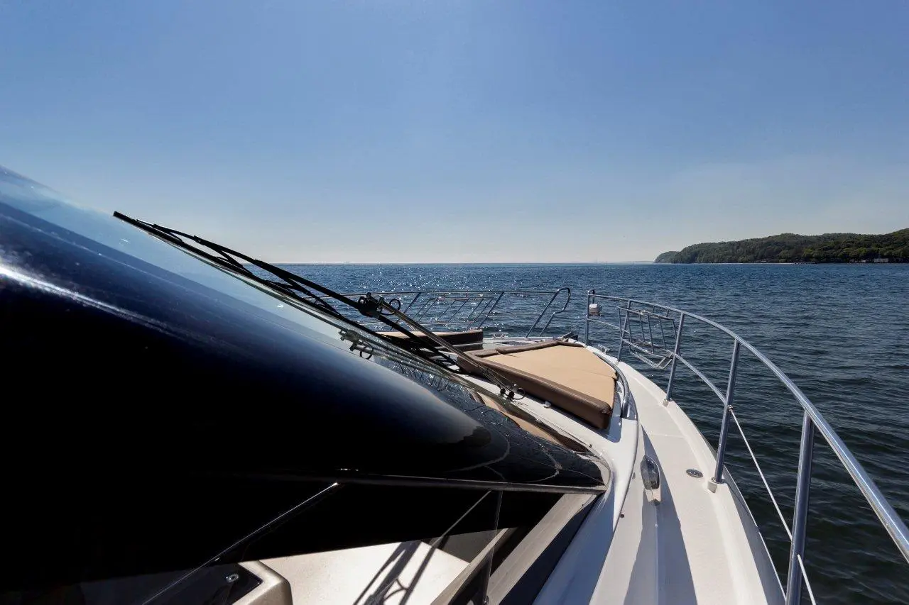View from the bow of a yacht overlooking calm blue waters, with the coastline visible in the distance under a clear sky.