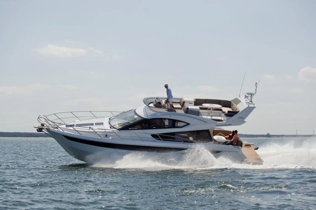 Luxury yacht cruising on calm waters, with two people onboard enjoying the sun and stylish seating area.