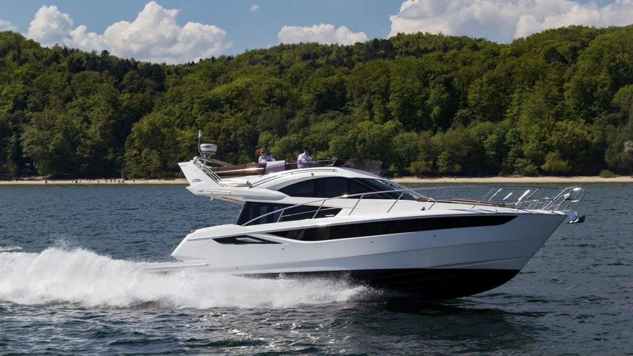A sleek white motorboat accelerates across a calm waterway, with two people enjoying the ride in the sunny backdrop.