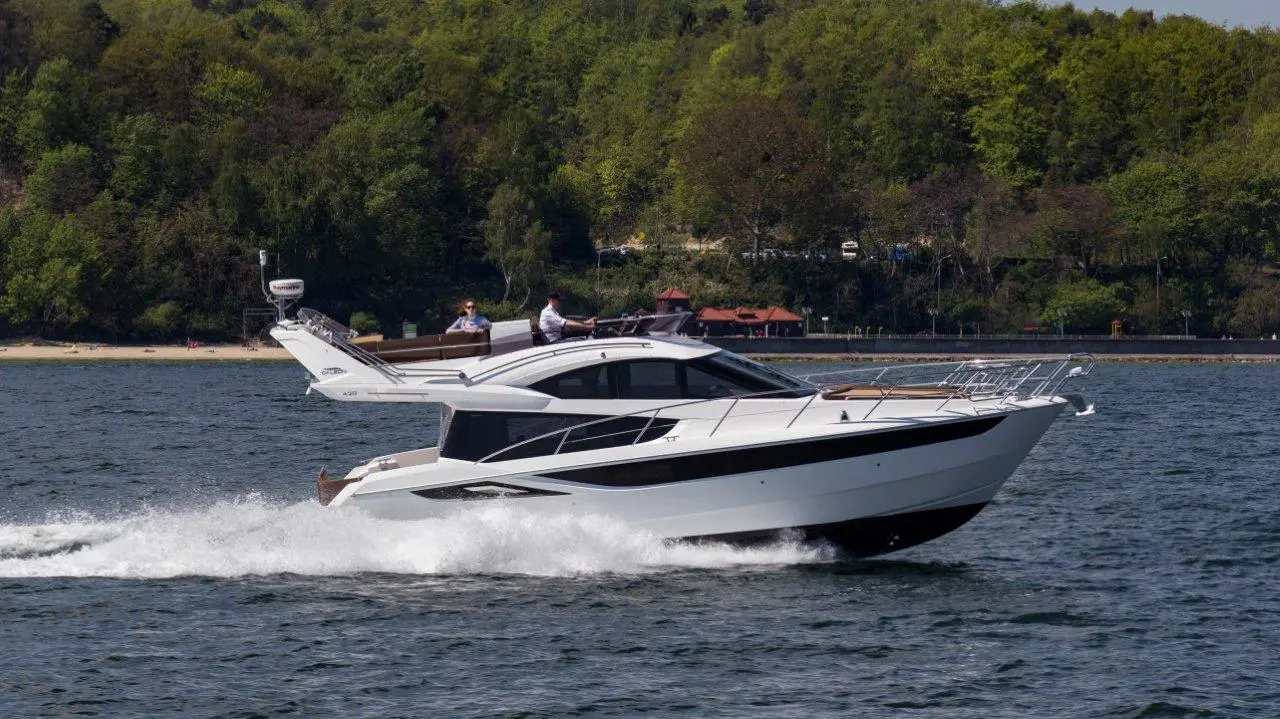 A sleek white motorboat navigates across blue waters with passengers enjoying the ride, surrounded by green forested banks.
