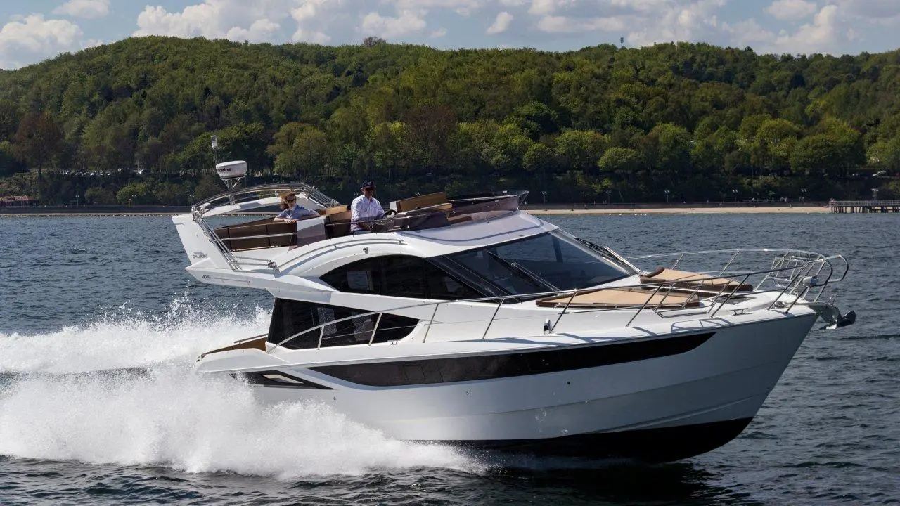 A sleek motorboat speeds across the water, with two men enjoying the ride against a lush green backdrop.