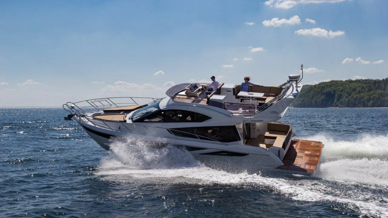 A sleek motor yacht speeds across the water with two people on board, enjoying a sunny day.