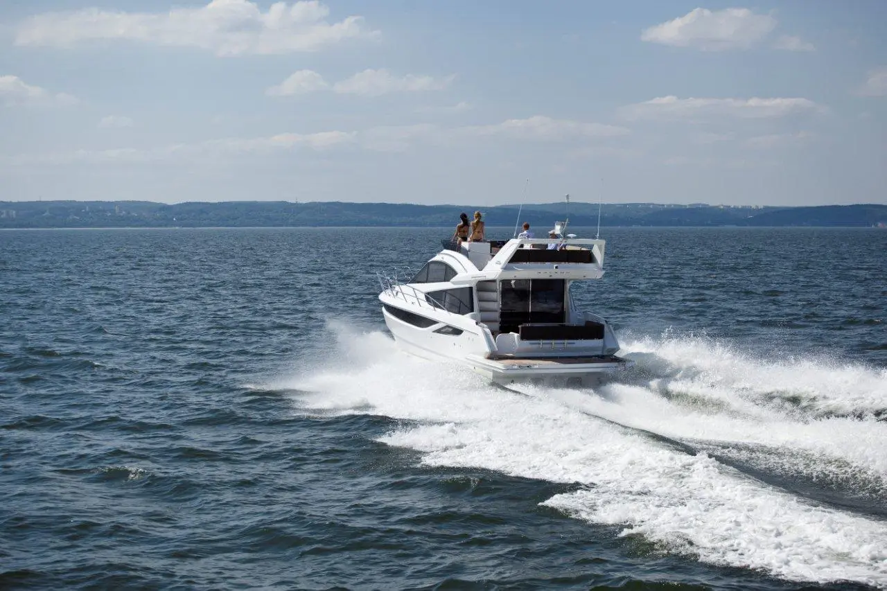 A white motorboat speeds across a sparkling blue lake, with people enjoying the sun on deck.
