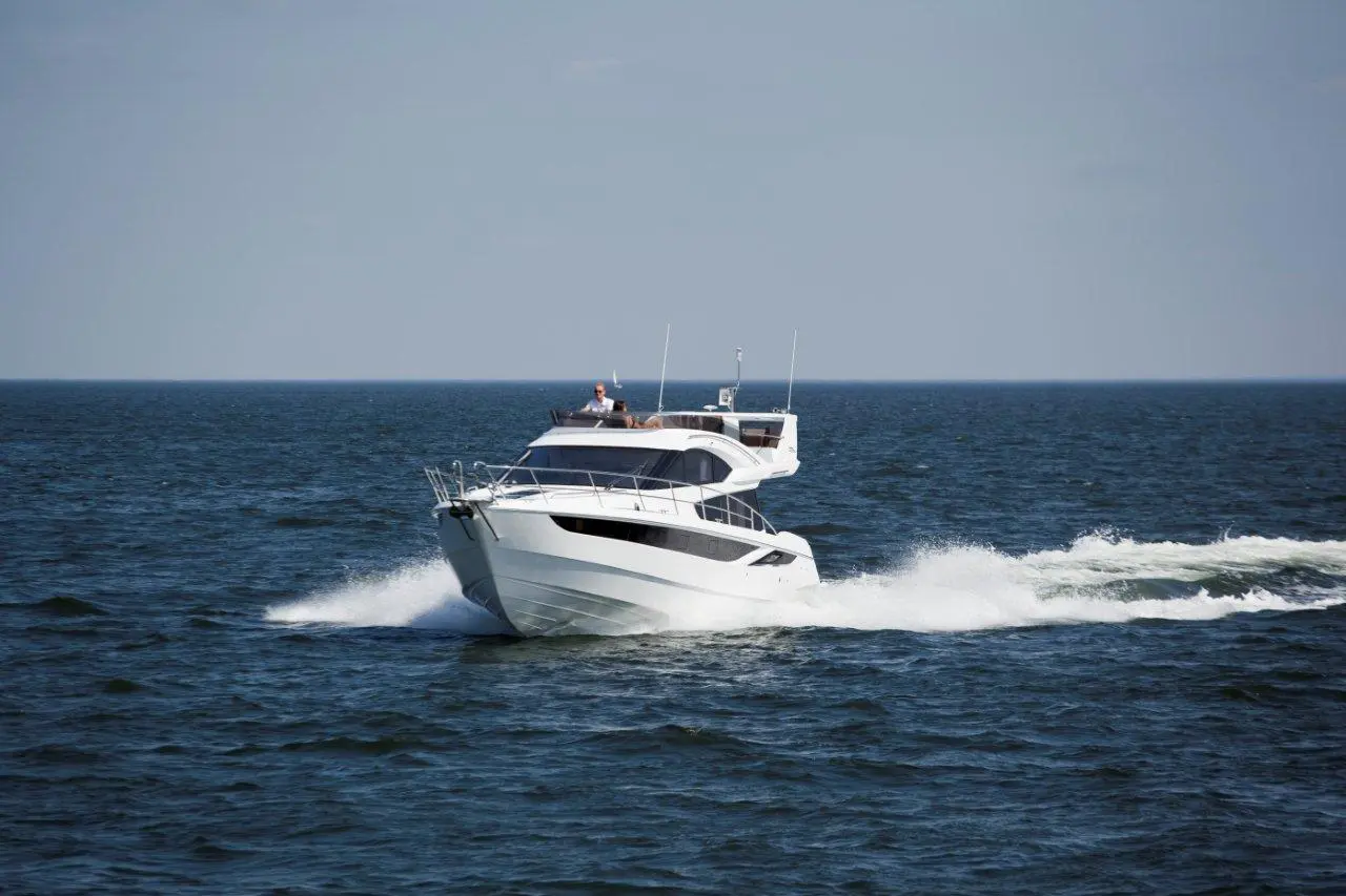 White motorboat cruising on calm sea, leaving a trail of frothy waves under a clear blue sky.