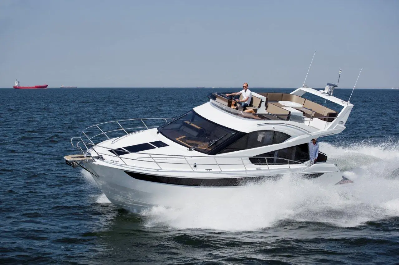 A sleek white motorboat speeds across blue water, with a man steering and another seated on the deck.