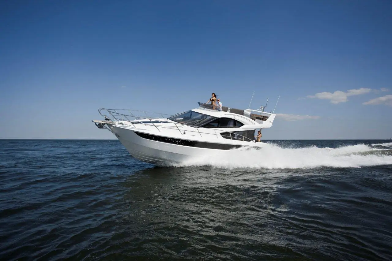 A sleek white motorboat speeds across calm waters, with people enjoying the ride against a clear blue sky.