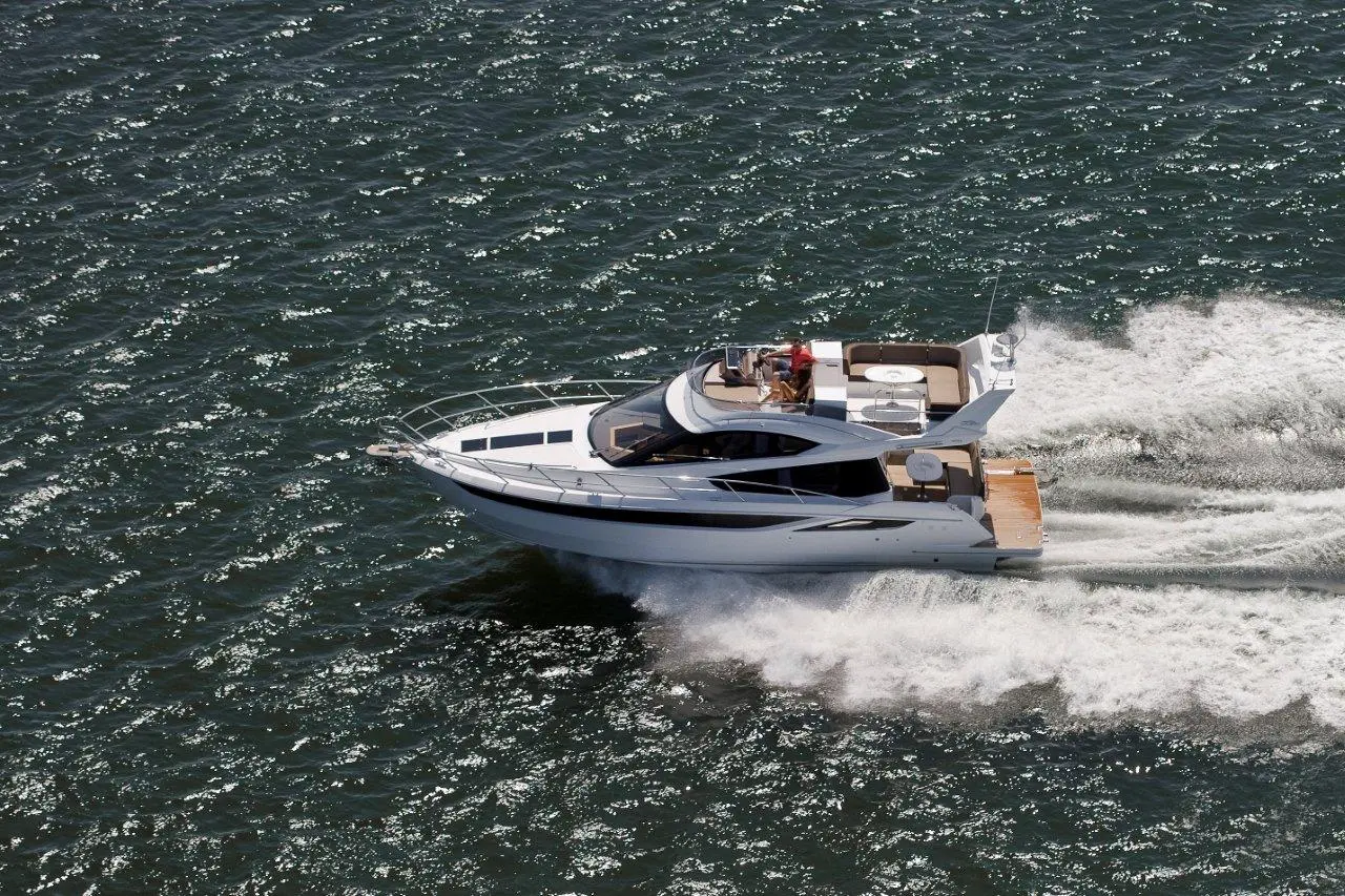 A white motor yacht speeds across sparkling blue water, leaving a wake, with a person at the helm enjoying the ride.