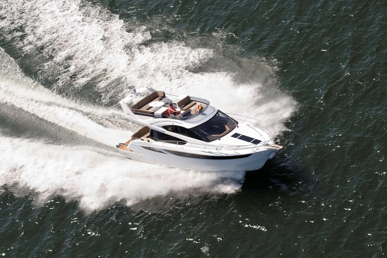 A luxury motorboat speeds across the water, leaving a trail of waves, with two people enjoying the ride on board.