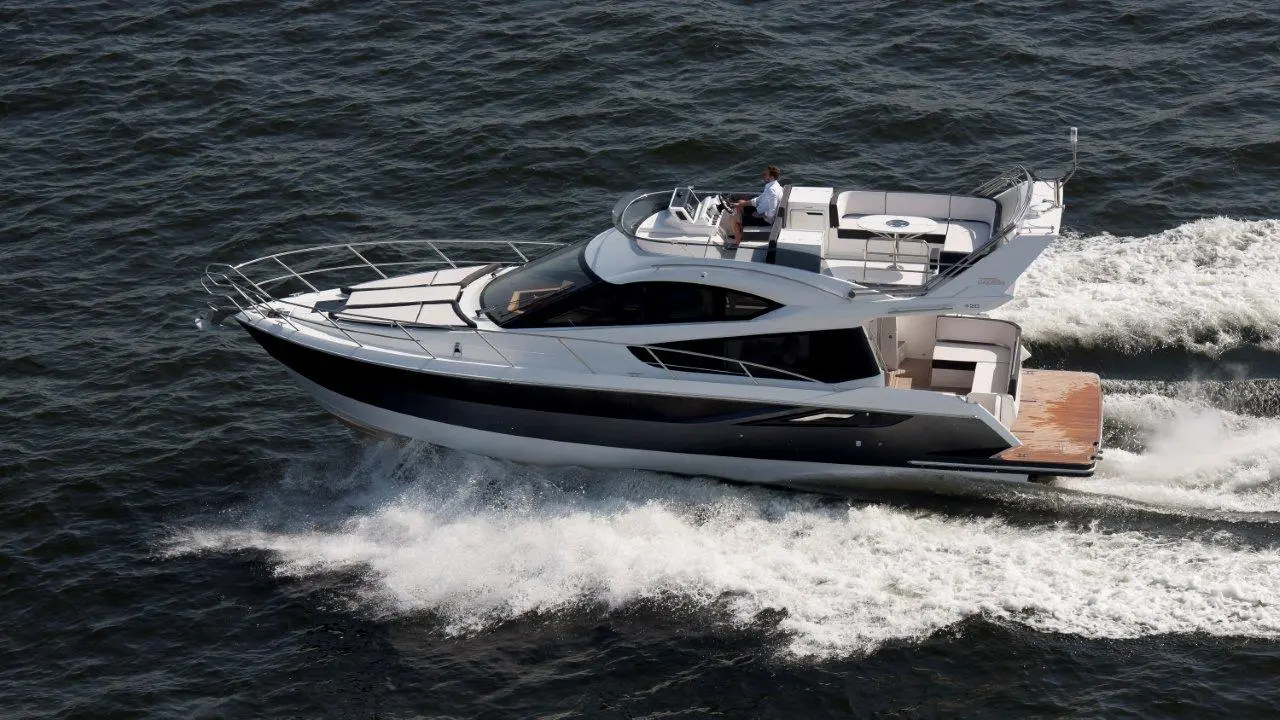 Luxury yacht cruising on water, with a captain at the helm and a spacious deck area for relaxation.