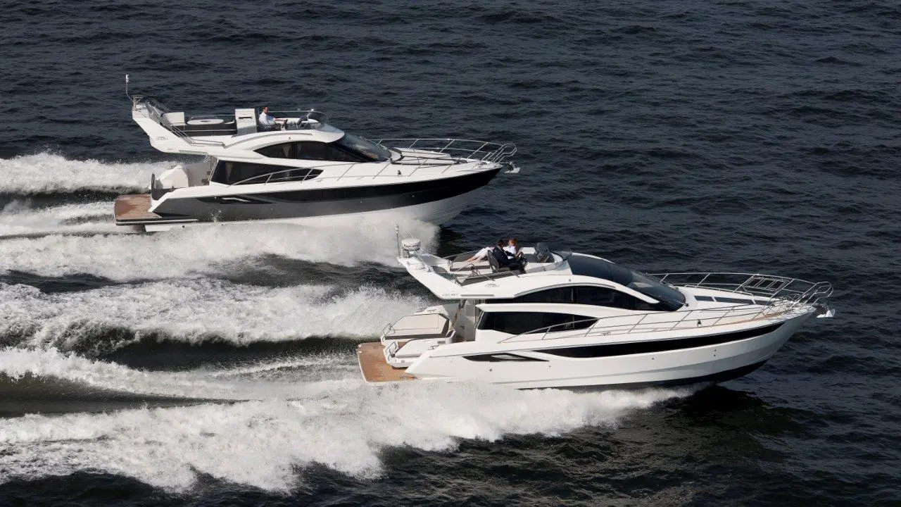 Two luxury motor yachts glide through ocean waves, creating frothy trails in the water under bright sunlight.