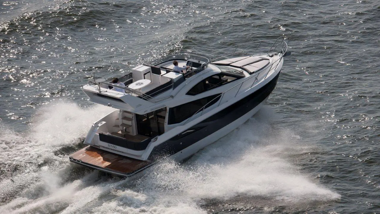 A sleek motorboat navigates sparkling water, leaving a trail of white foam, with passengers visible on the upper deck.