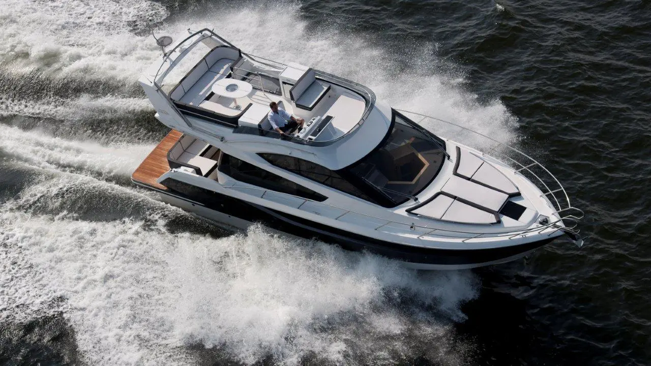 A white motorboat with a man at the helm, creating waves as it speeds through water under sunlight.