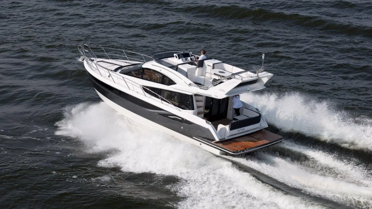 A sleek motorboat with a white and black design glides across choppy water, creating a wake. Two people are onboard.