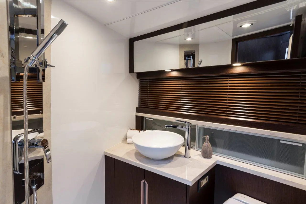 Modern bathroom featuring a sleek sink, tiled shower, wooden blinds, and contemporary fixtures in a bright space.