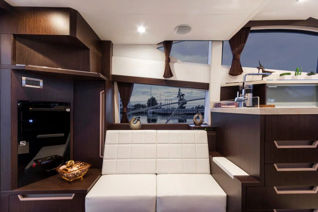 Modern boat interior featuring a white bench, dark wood cabinetry, and large window with river view. Decorative items included.