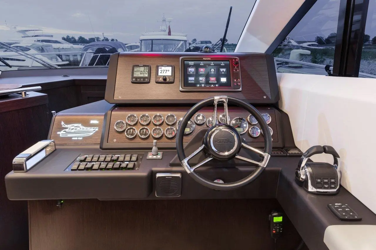 Luxury yacht control panel featuring a steering wheel, digital screens, gauges, and communication devices, with boats in the background.