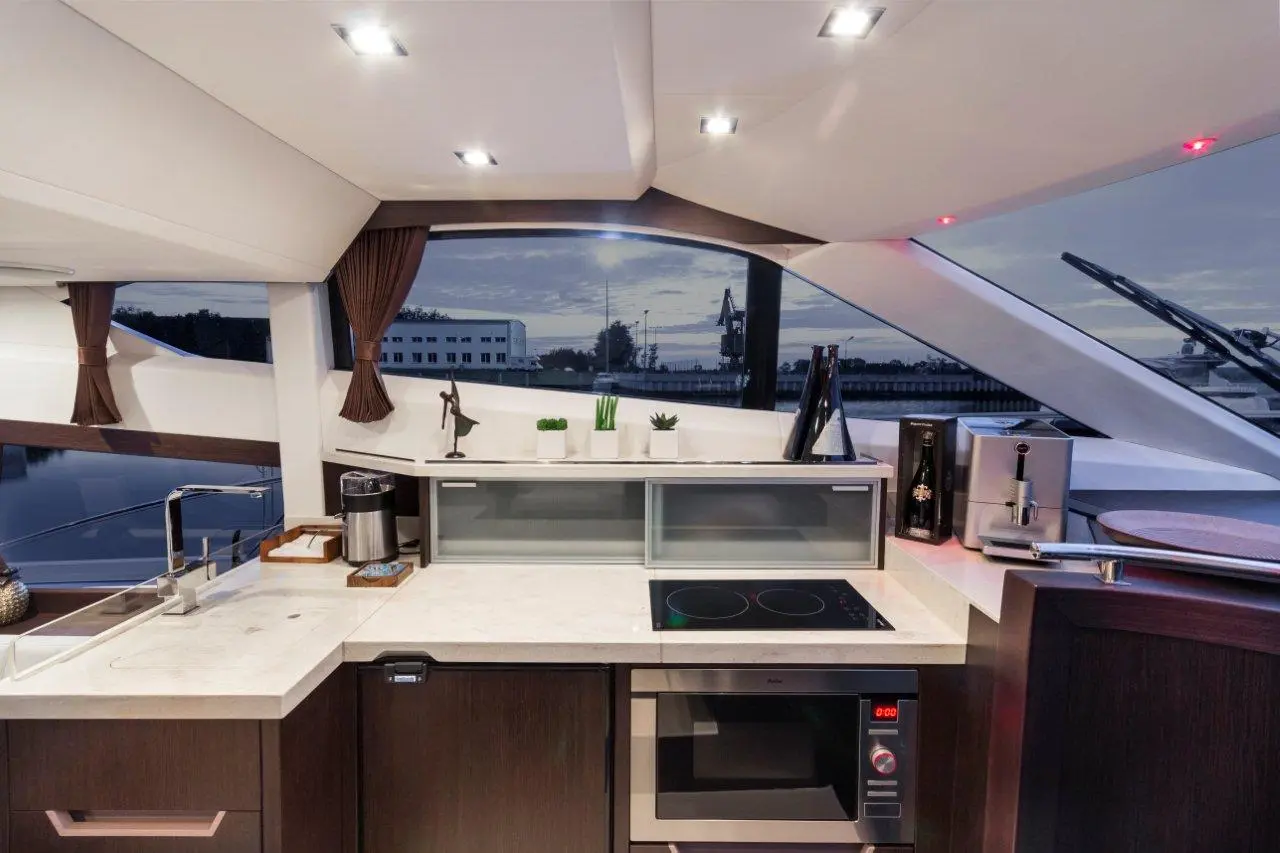 Modern yacht kitchen interior with a countertop, microwave, induction cooktop, coffee maker, and scenic window view.
