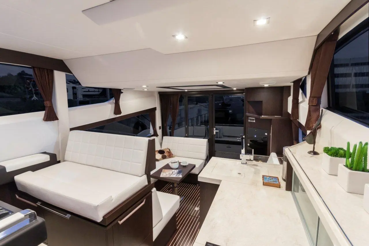 Modern boat interior with white seating, dark cabinetry, and large windows, showcasing a sleek, comfortable lounge area.