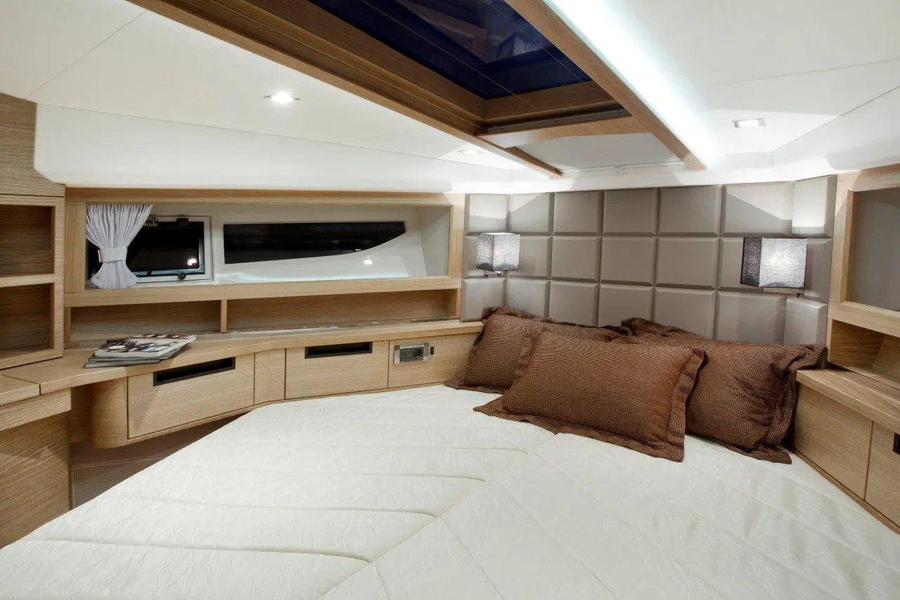 Modern yacht bedroom featuring a large bed with white linens, wooden storage, soft lighting, and a window with curtains.
