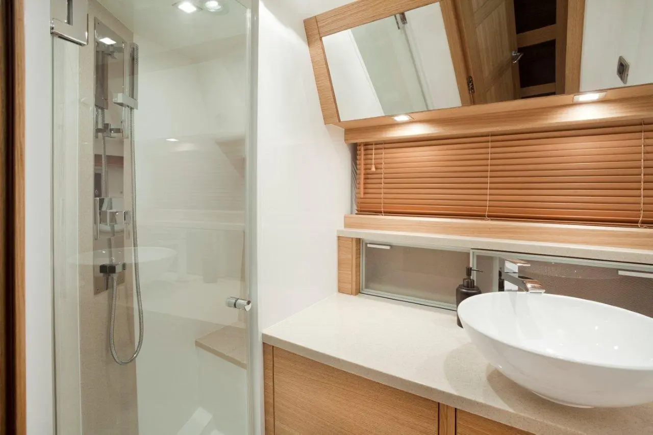 Modern bathroom featuring a glass shower, oval basin, wooden cabinetry, and soft lighting, creating a sleek, minimalist style.