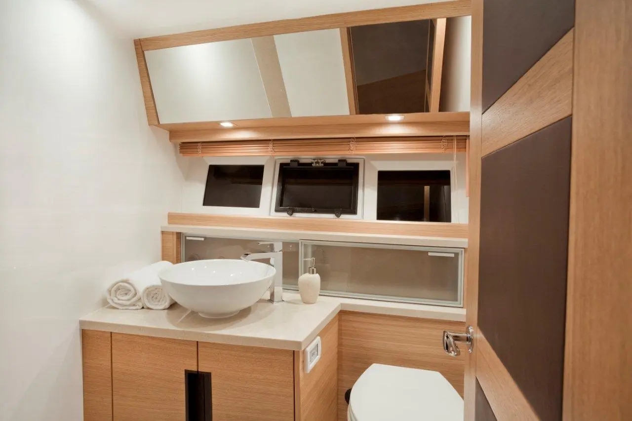 Modern bathroom featuring a round basin, wooden cabinetry, a toilet, and windows, illuminated by soft lighting.
