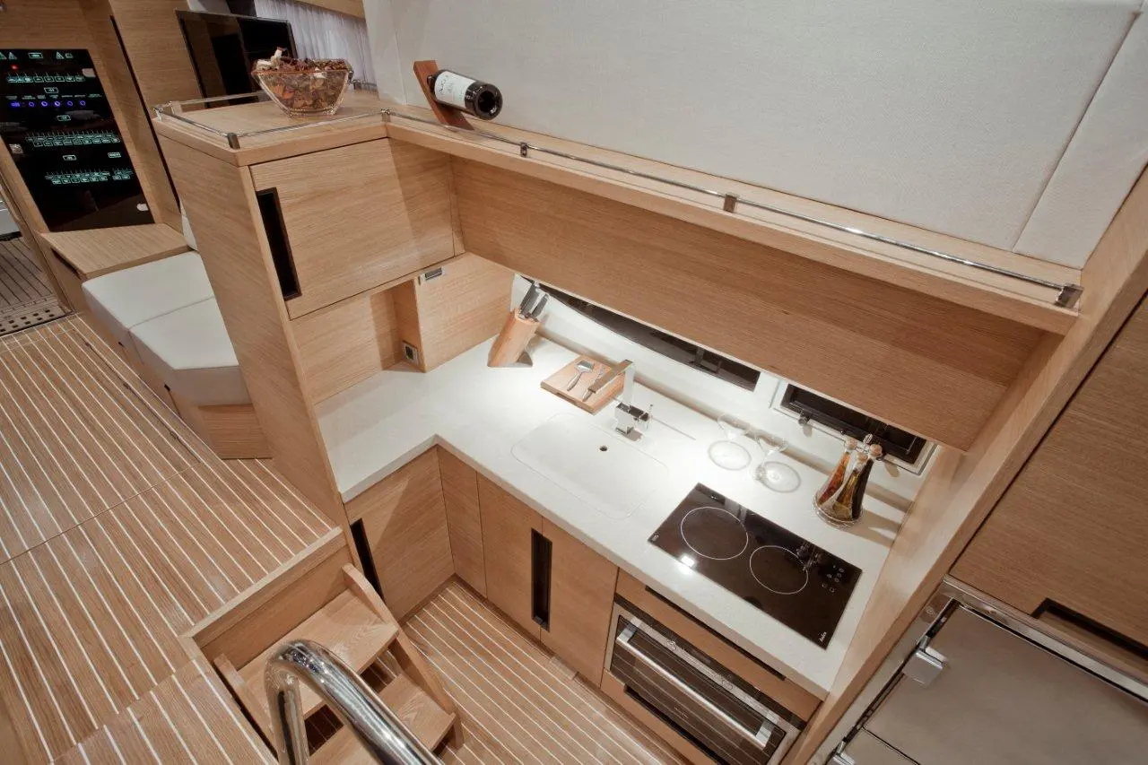Modern yacht kitchen featuring wooden cabinetry, a countertop with a sink, stovetop, glassware, and a wine bottle on display.