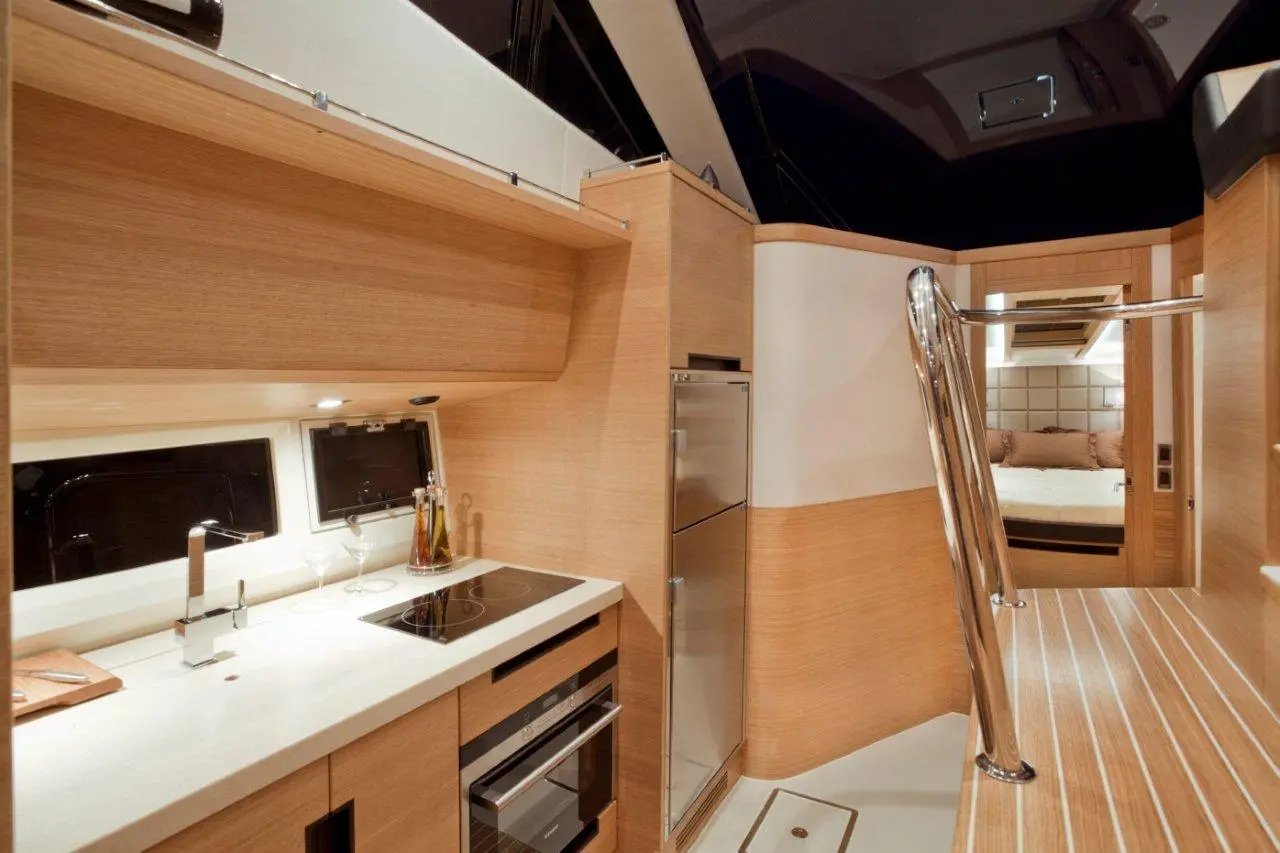 Modern yacht galley with wooden cabinets, stainless steel appliances, a sleek countertop, and a glimpse of a cosy cabin.