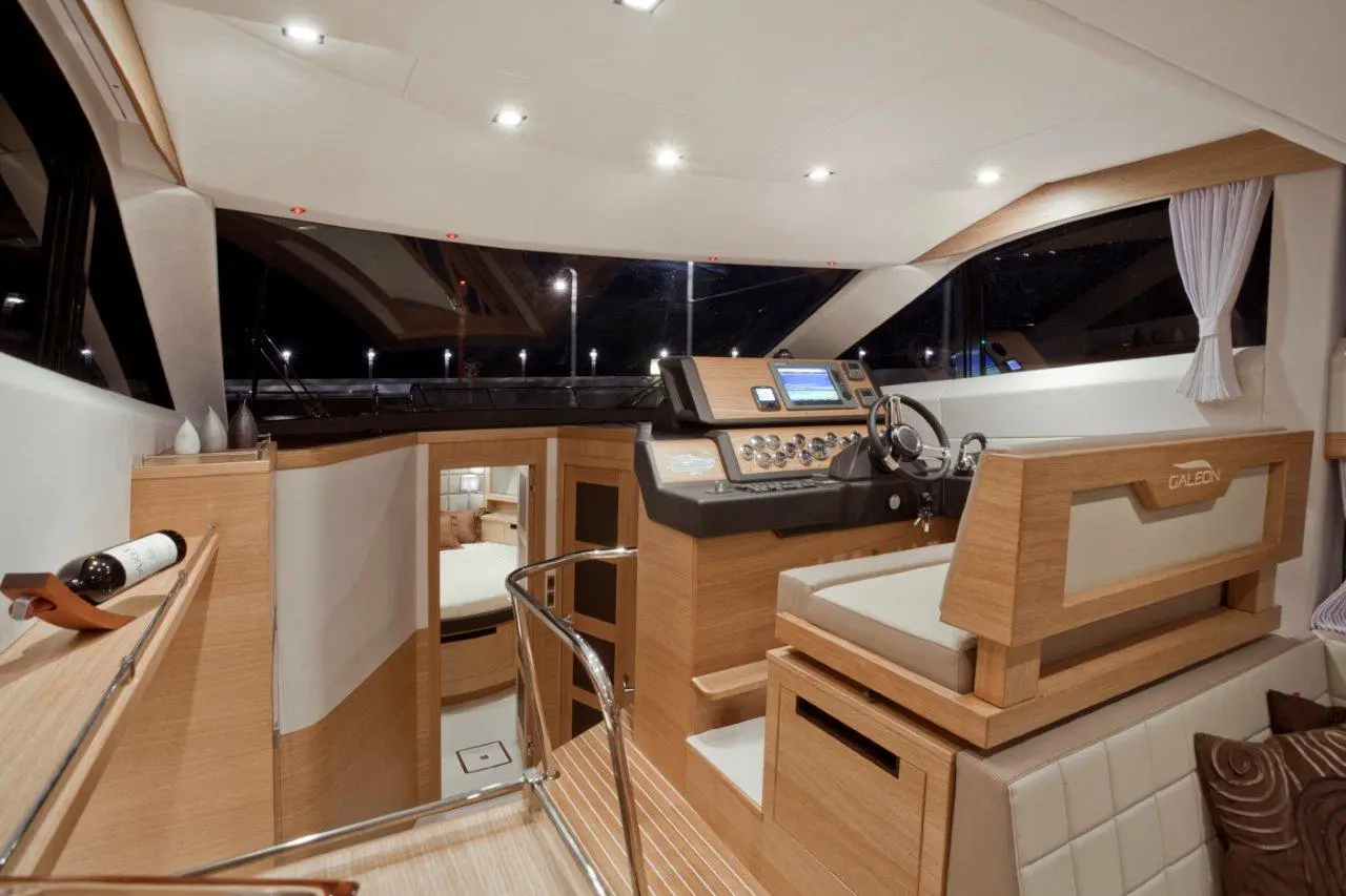 A modern yacht's interior helm, featuring a steering wheel, control panel, leather seating, and wood finishes, exudes luxury.