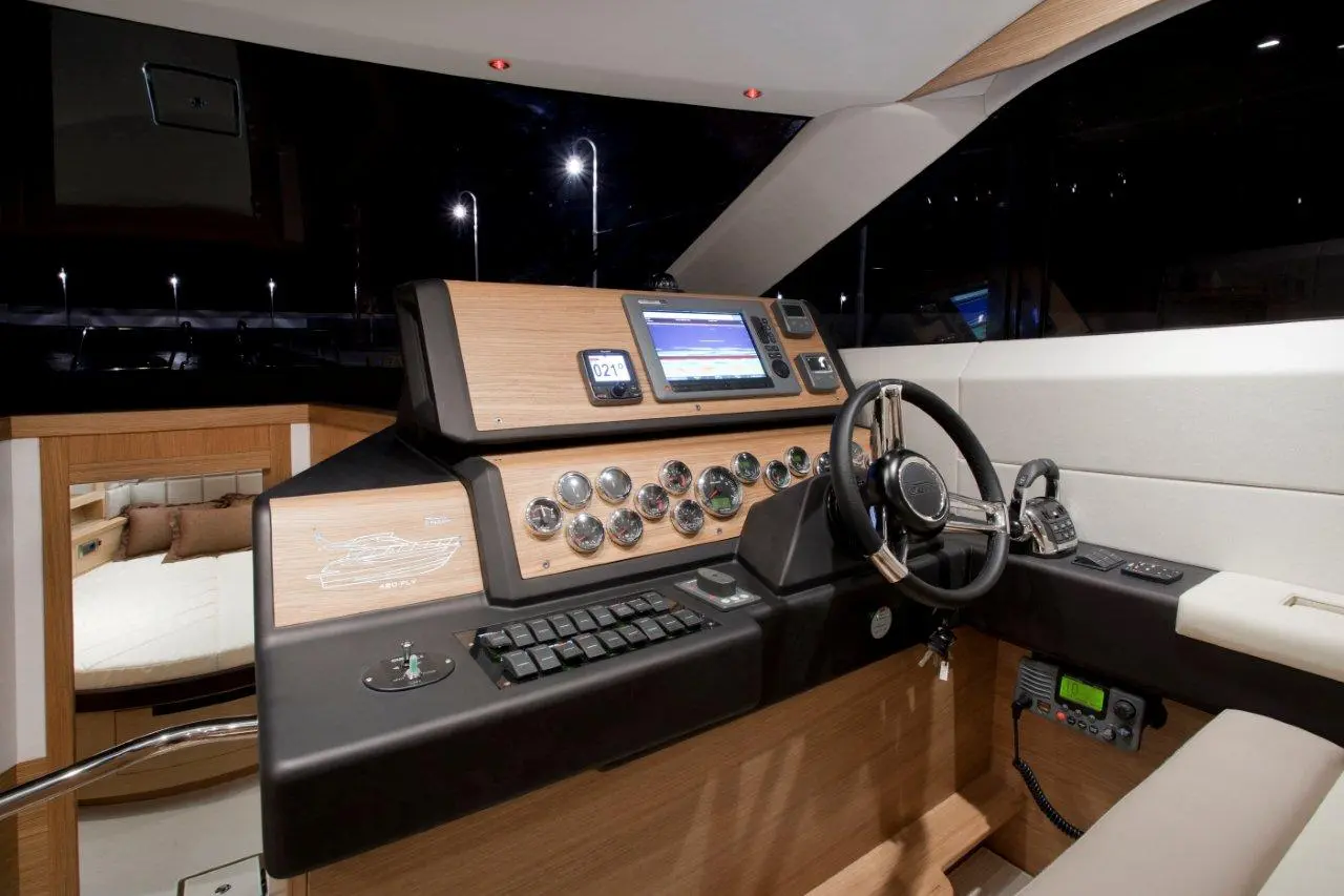 Luxury boat dashboard featuring wooden details, navigational screens, dials, and the steering wheel, with a cabin view in the background.