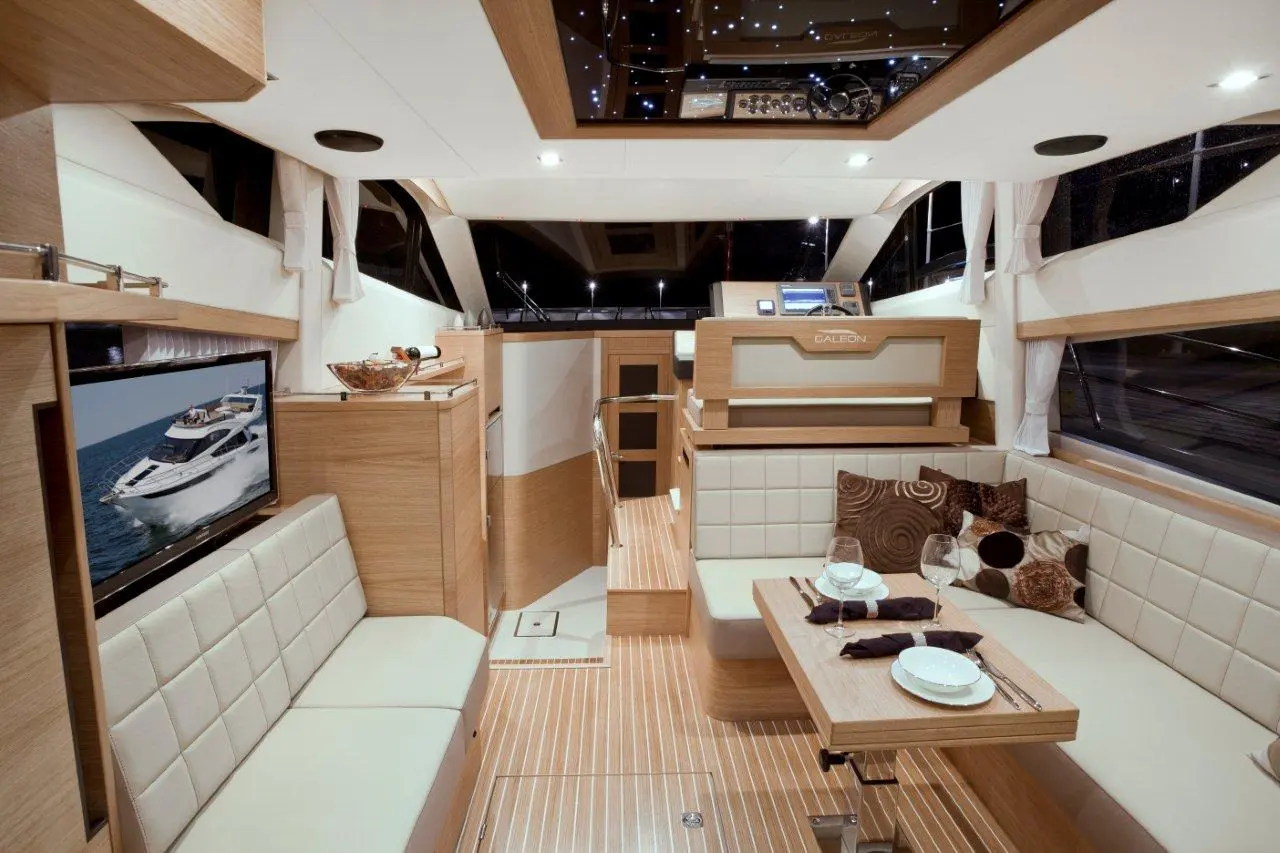 Luxury yacht interior featuring a modern saloon with beige couch, dining table set, and nautical-themed decor.