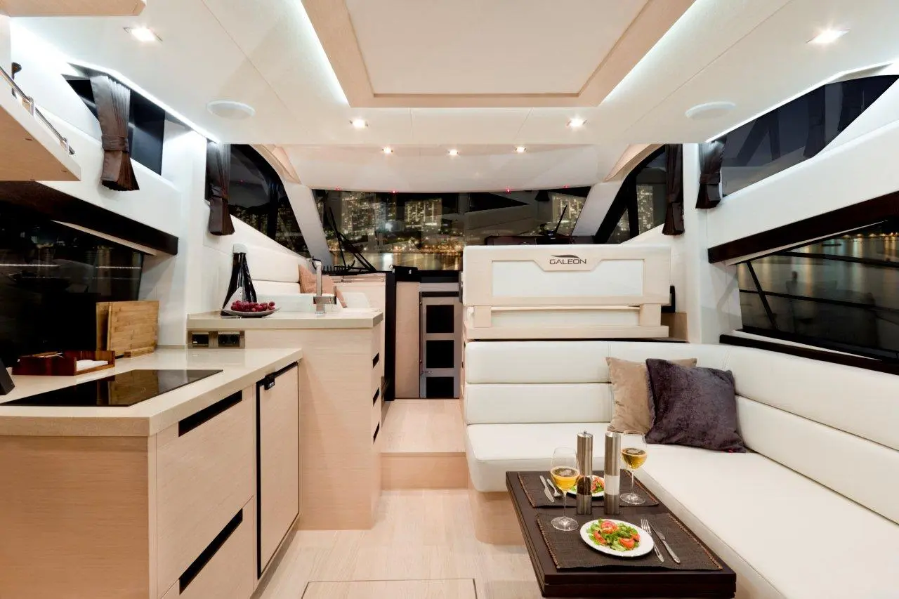 Modern yacht interior with sleek furniture, dining setup, and city skyline views through large windows. 제품명: GALEON.