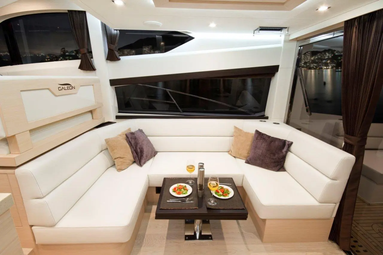 Luxurious yacht interior featuring a cozy seating area with plates of salad, drinks, and a view of a city at night.