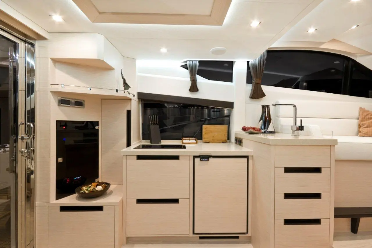 Modern yacht kitchen with white cabinetry, a sink, stovetop, and a bowl of snacks on the counter, showcasing luxury design.