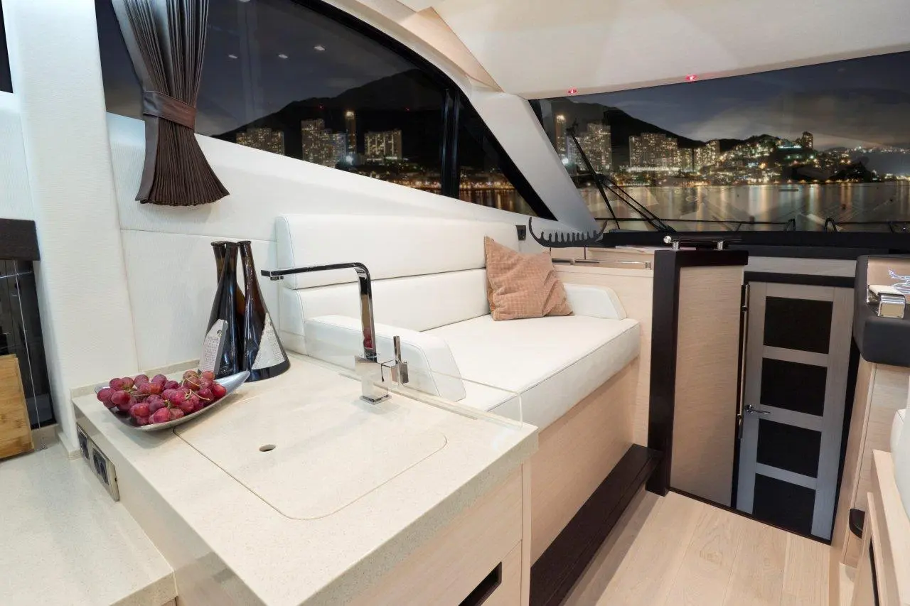 Modern yacht interior with a white sofa, grape bowl, and sleek kitchen faucet, showcasing a city skyline at night through large windows.