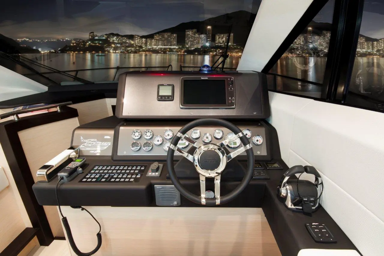 Luxury yacht cockpit featuring a sleek steering wheel, electronic control panel, and a panoramic view of city lights.