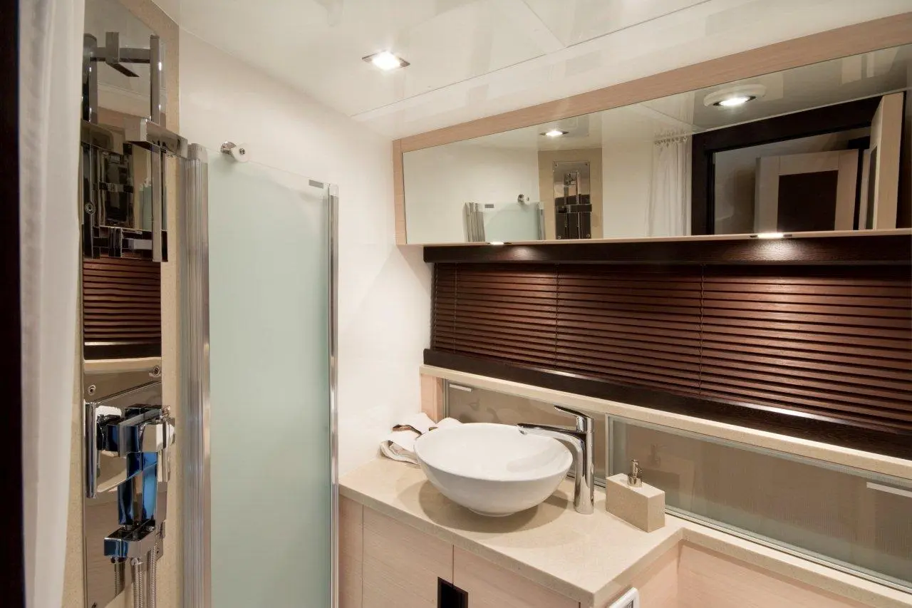 Modern bathroom featuring a glass shower, round sink, wooden blinds, and minimalist design elements with neutral tones.