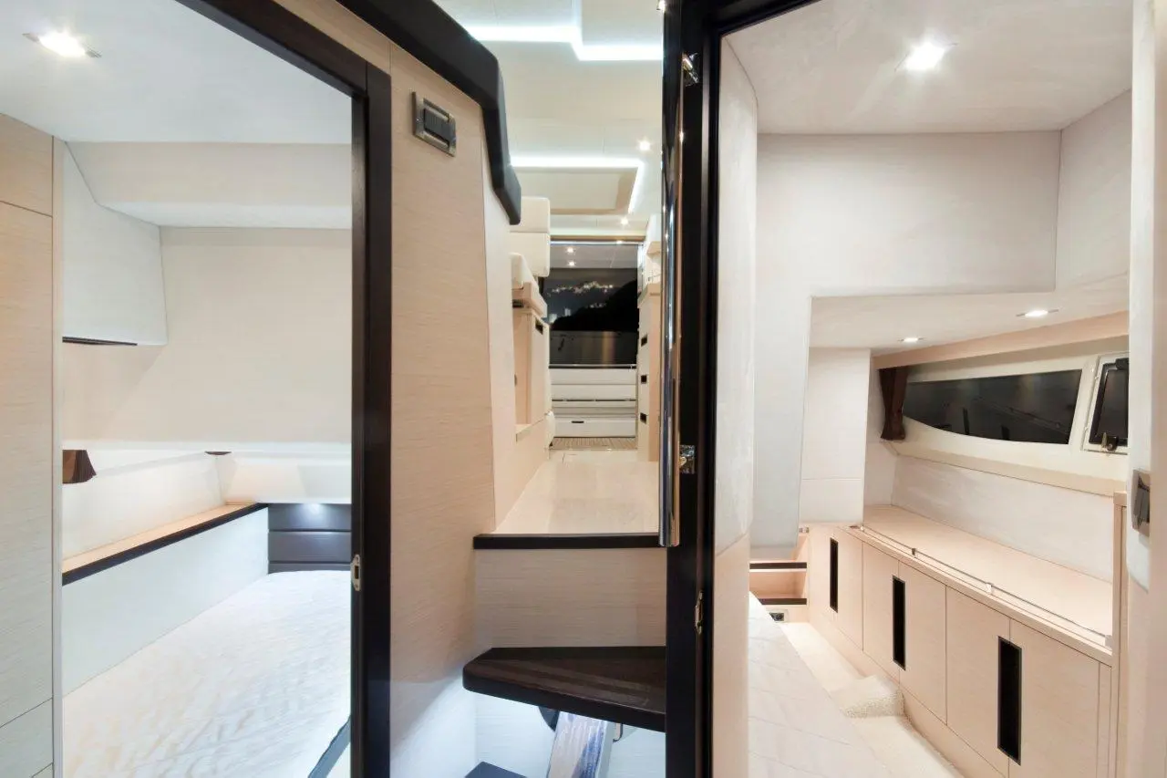Interior view of a modern yacht showing two rooms, sleek cabinetry, plush bedding, and ambient lighting in a bright space.