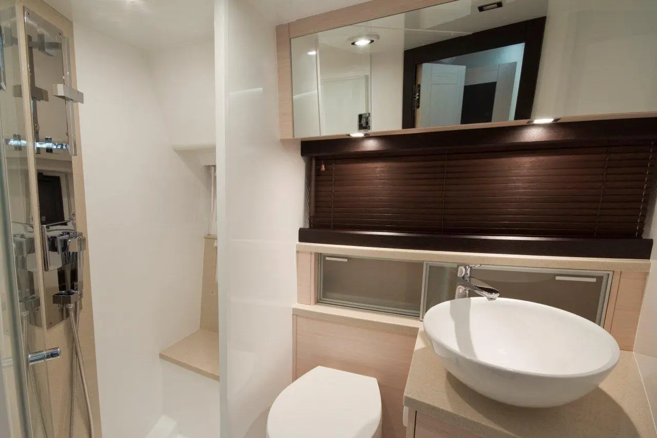 Modern bathroom featuring a white vessel sink, toilet, shower area, and wooden blinds for privacy.