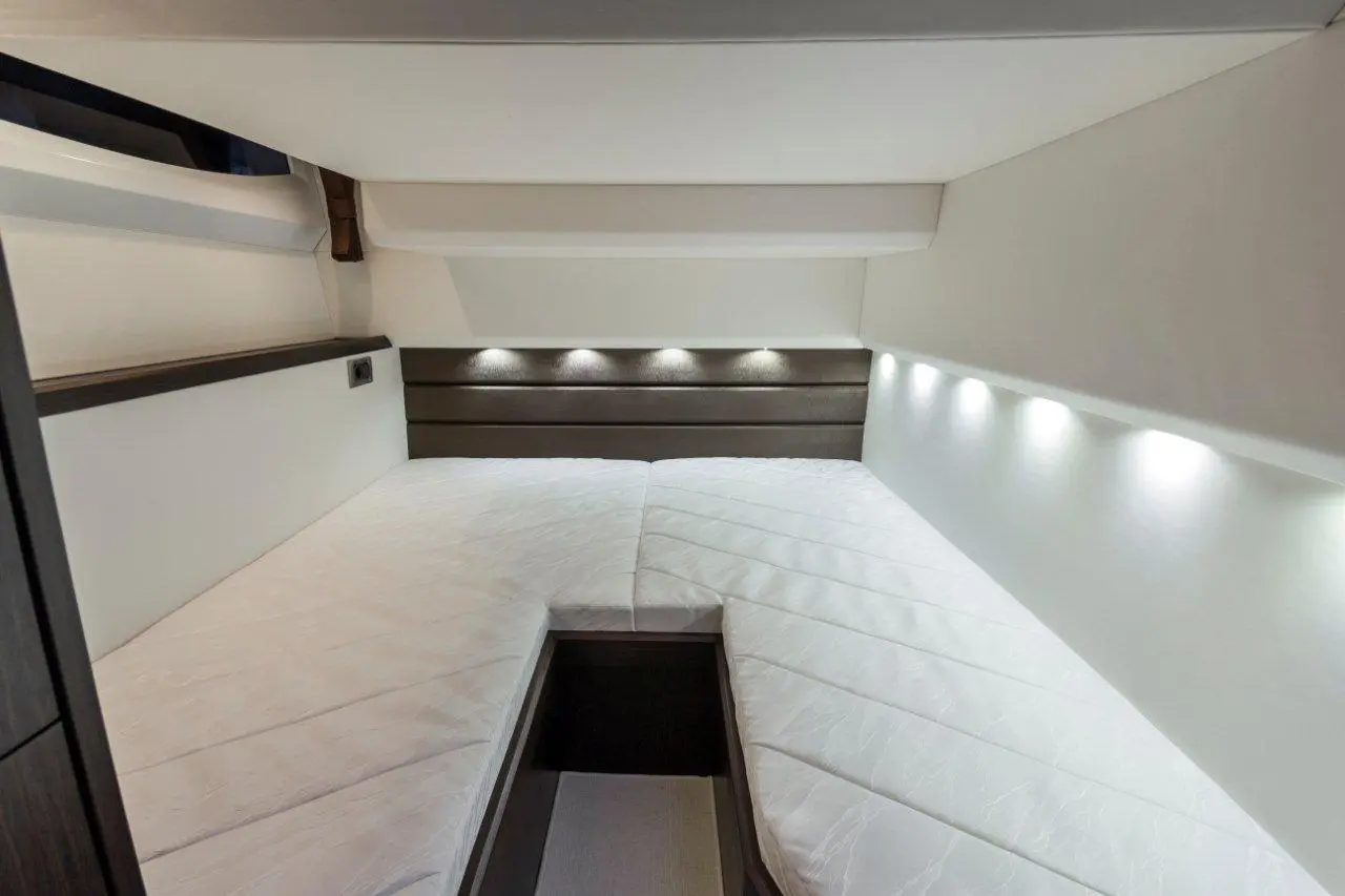 Cozy interior of a yacht cabin featuring a double berth, white bedding, and soft LED lighting along the walls.