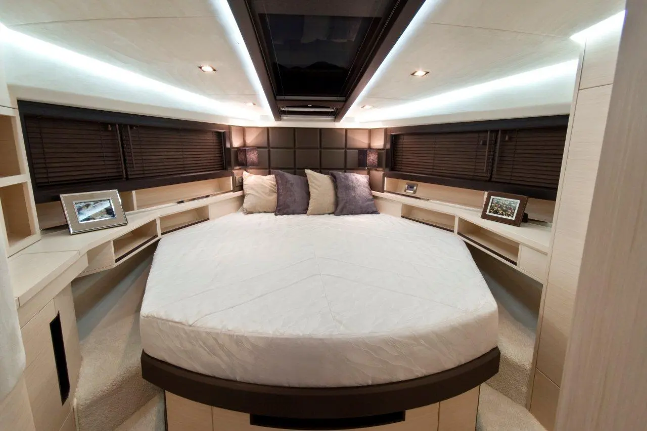 Modern yacht bedroom featuring a circular bed, soft lighting, two lamps, and built-in shelves with decorative frames.